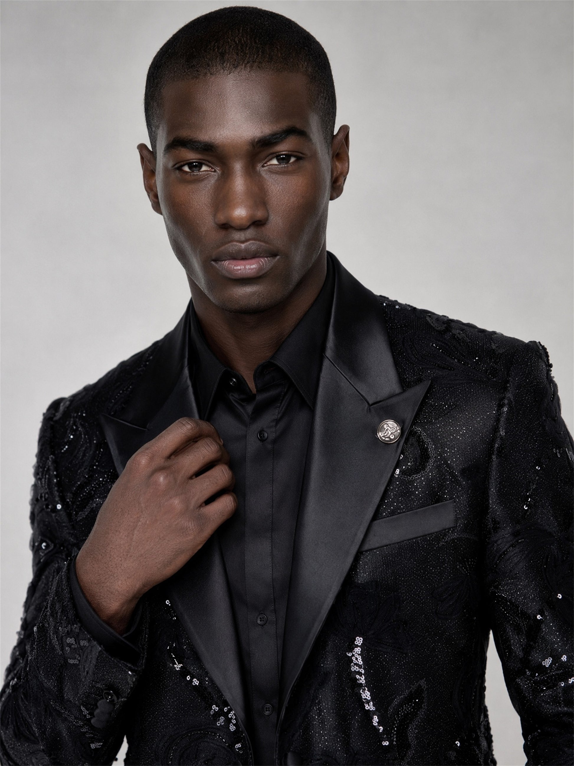 Savile black sequin floral suit – close-up face and lapel, silver medallion brooch and satin peak lapel detail