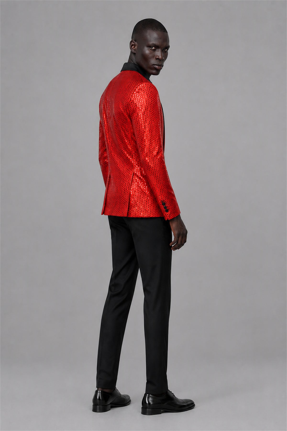 Savile Red Sequin Tuxedo Jacket – Full front standing view, hand on button showing slim-fit silhouette and red sequin embellishment with black satin lapel