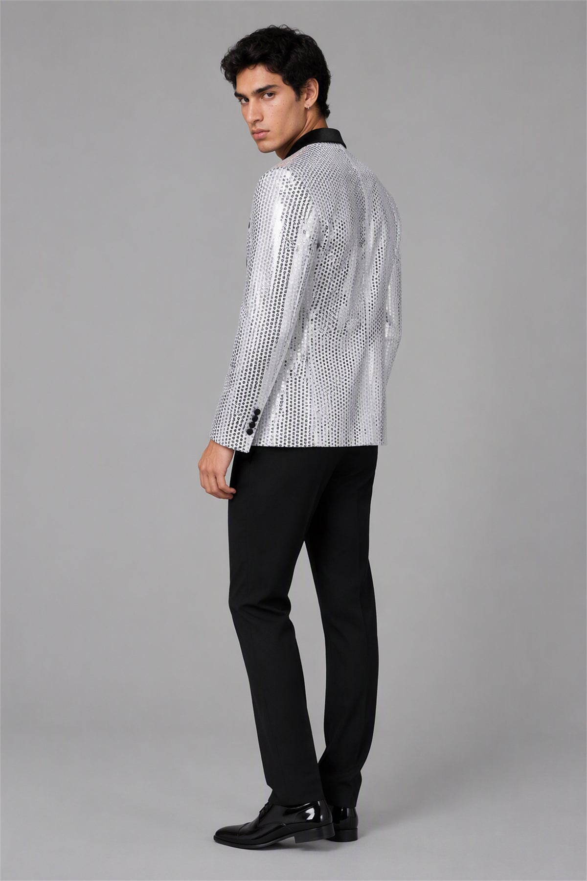 Savile Silver Sequin Tuxedo Jacket – Full front walking view showing all-over mirror silver sequin jacket with black satin peak lapel, black shirt and black trousers