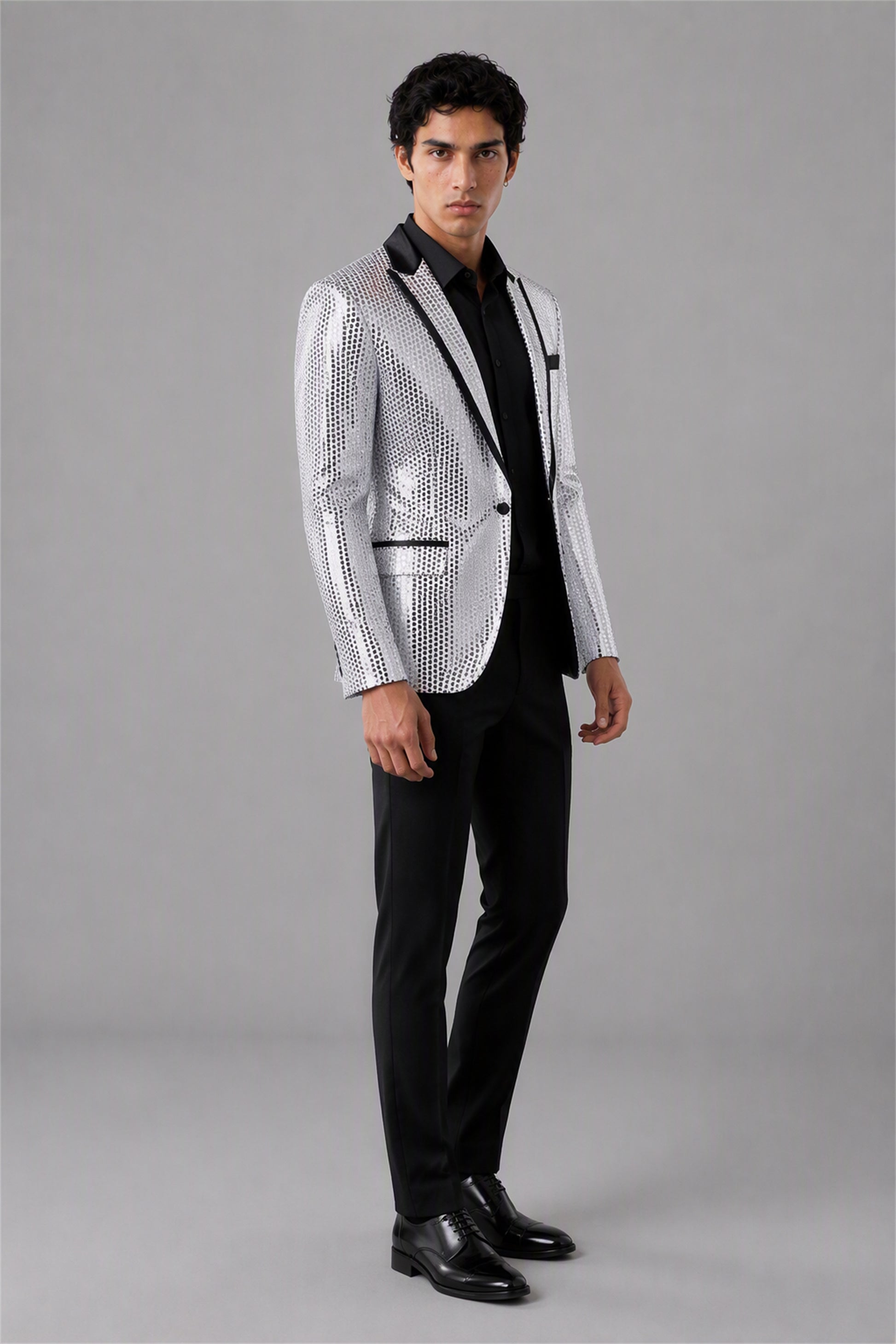 Savile Silver Sequin Tuxedo Jacket – Three-quarter front view, model holding jacket showing silver sequin texture and black satin lapel detail