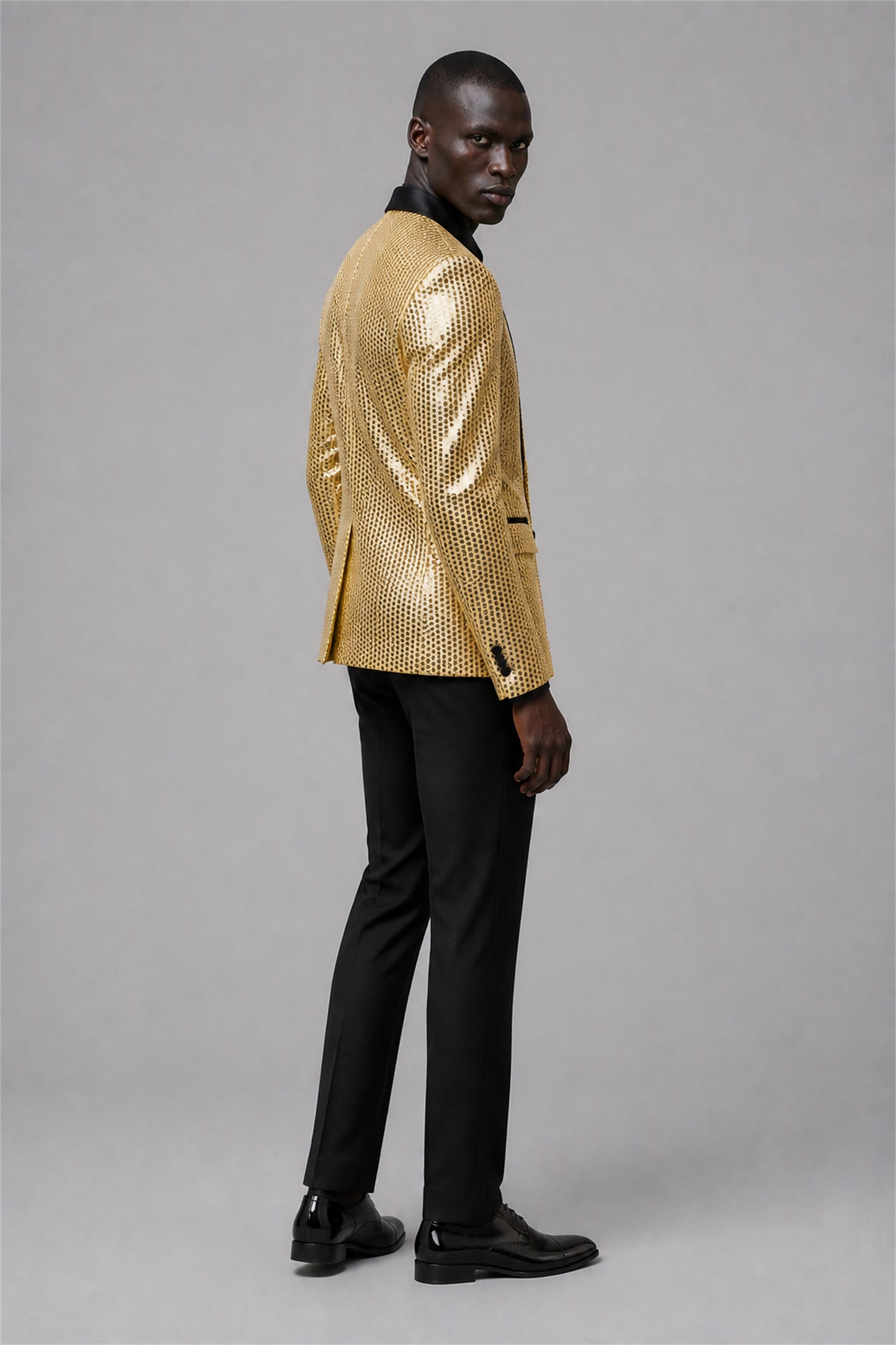 Savile Gold Sequin Tuxedo Jacket – Full front standing view, hand in pocket showing slim-fit silhouette and gold sequin embellishment with black satin lapel