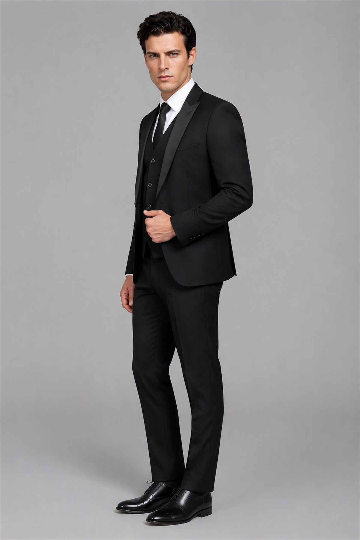 Savile Black 3-Piece Tuxedo Set – Three-quarter side view, hand on jacket showing slim-fit silhouette, shawl lapel profile and white shirt styling